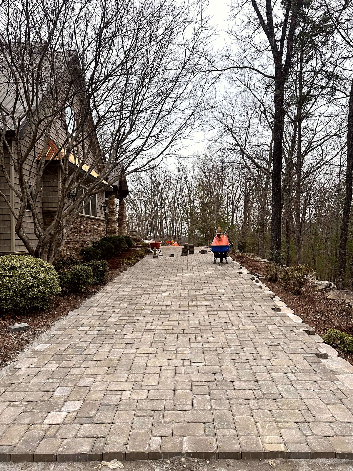Paver driveway installation in progress at a wooded home