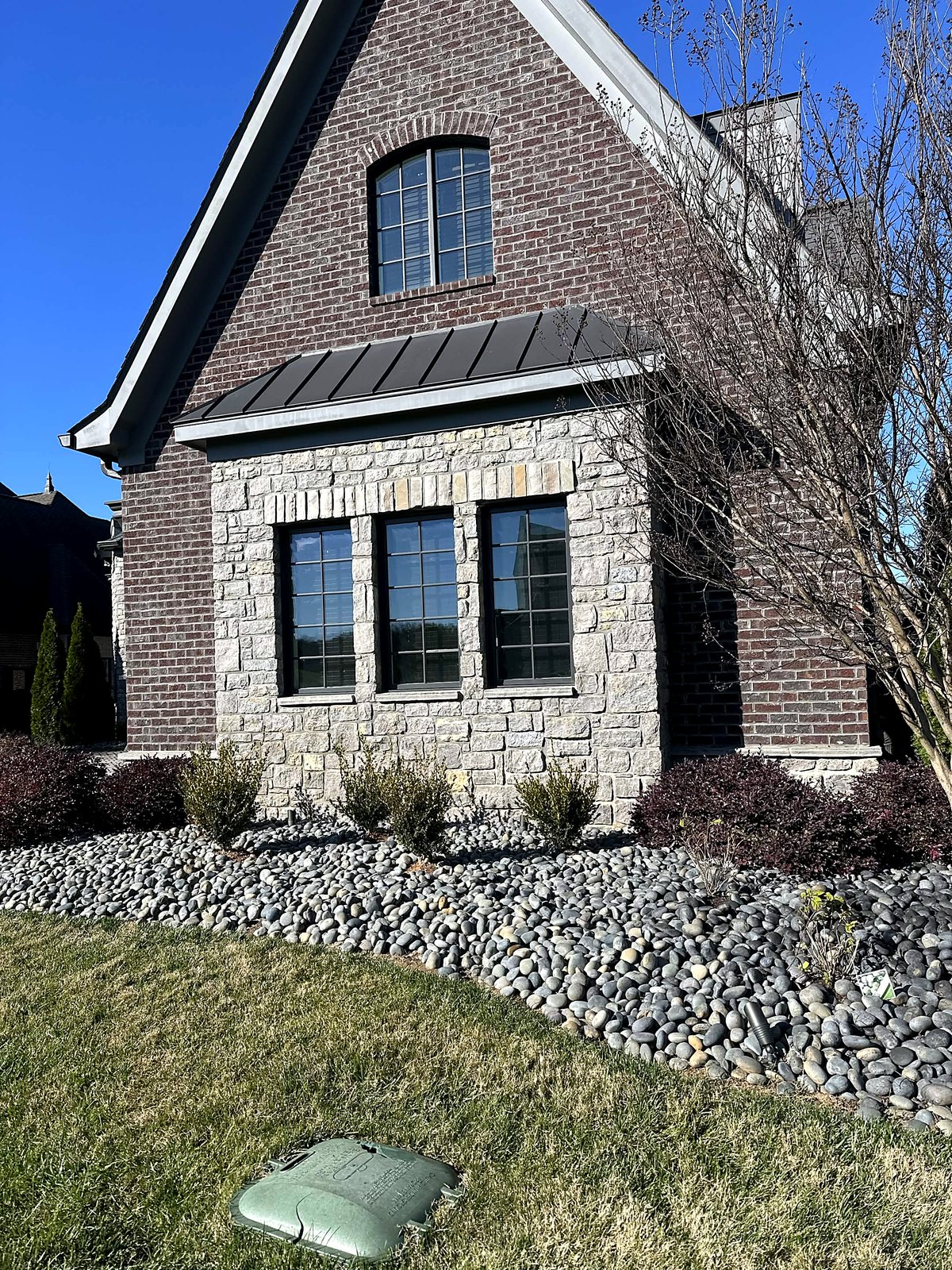 River rock bed with shrubs against a brick and stone home